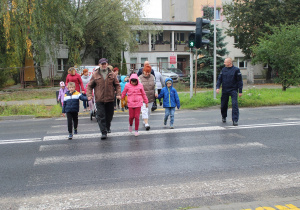 Przedszkolaki podczas przechodzenia przez ulicę pod opieką funkcjonariusza Policji i wychowawców